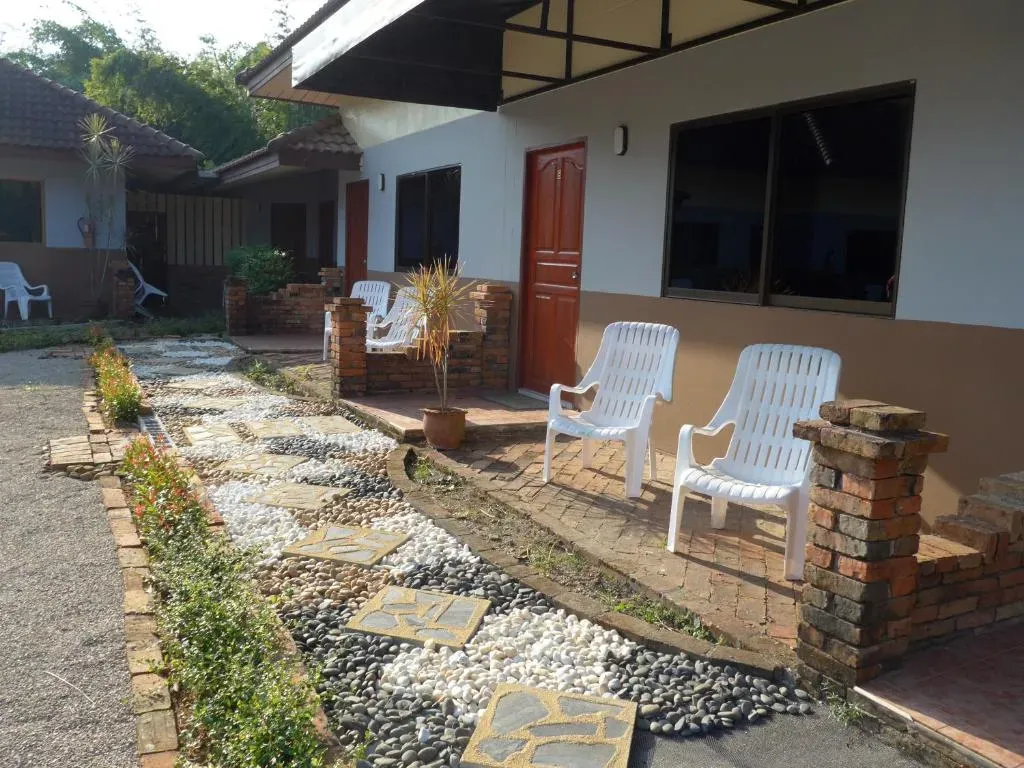 Landscaped garden path with decorative pebbles and white chairs beside hotel bungalows